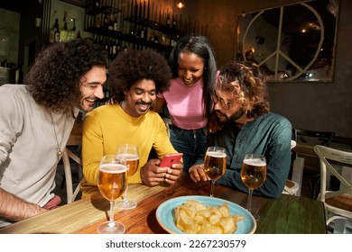 Group portrait multi-ethnic friends group watching smiling at cell phone at bar after work at pub happy hour. Colleagues having fun together drinking alcohol indoors. People and social networking. - Powered by Shutterstock