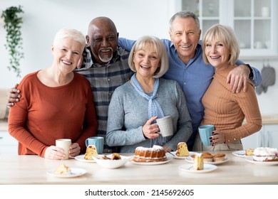 Group portrait of multiracial senior friends enjoying time together at home. Happy elderly men and women drinking tea and eating cake, having party, embracing and smiling at camera, kitchen interior - Powered by Shutterstock