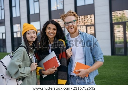Group portrait of multiracial smiling students with books and backpacks looking at camera walking in university campus. Education concept