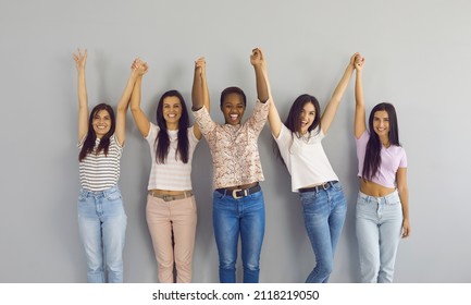 Group Portrait Of Positive Confident Diverse Ladies Holding Hands. Team Of Happy Excited Beautiful Young Women Standing Together By Studio Wall, Raising Hands Up And Smiling. Female Community Concept