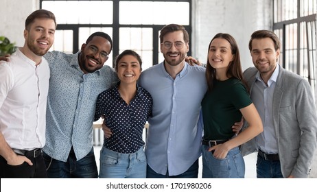 Group Portrait Of Smiling Diverse Multiracial Businesspeople Look At Camera Posing In Office Together, Happy Multiethnic Young Colleagues Hug Show Unity And Support, Teamwork, Leadership Concept