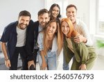 Group portrait of smiling friends, students or colleagues in casual clothes standing together, hugging each other and looking at camera. Happy young people making group photo during weekend hangout.