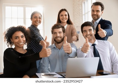 Group portrait of smiling multiracial young businesspeople sit at desk in office show thumbs up together, happy diverse colleagues recommend good quality corporate service, acknowledgment concept - Powered by Shutterstock