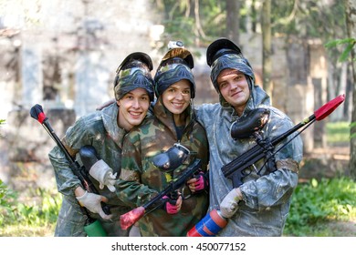Group portrait of three smiling paintball players outdoors