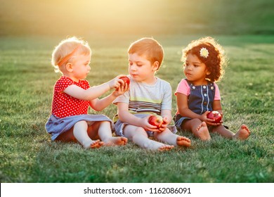 Group Portrait Of Three White Caucasian And Latin Hispanic Children Boy And Girls Sitting Together Sharing And Eating Apple Food. Love Friendship Childhood Concept. Best Friends Forever.