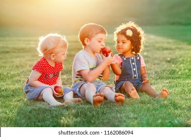 Group Portrait Of Three White Caucasian And Latin Hispanic Children Boy And Girls Sitting Together Sharing And Eating Apple Food. Love Friendship Childhood Concept. Best Friends Forever.