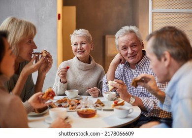 Group of positive aged friends sitting at table and laughing while drinking tea and eating pizza together in cafe - Powered by Shutterstock