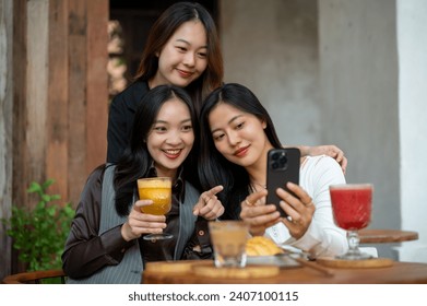 Group of positive and beautiful Asian female friends are enjoying chit chat, gossiping, looking online contents on a smartphone while hanging out at a cafe in the city together. - Powered by Shutterstock