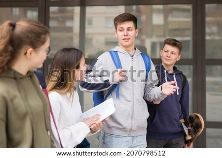 Group of positive cheerful teenagers hanging out on streets of city on warm sunny day