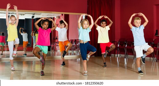 Group of positive childrens trying balance movements of ballet in a classroom