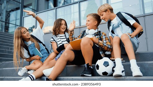 Group of positive diverse classmates greet each other high five in sitting on the stairs near school building and prepare to study, outdoors. Young caucasian school friends studying outdoor - Powered by Shutterstock