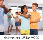 Group of positive juvenile boys and girls doing Tango poses in training room during workout session