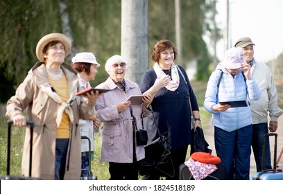 A Group Of Positive Senior Elderly People Travelers Using Tablets Waiting For Train Before Going On A Trip

