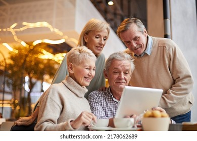 Group of positive senior friends in casual clothing using tablet while surfing websites in cafe with wifi - Powered by Shutterstock