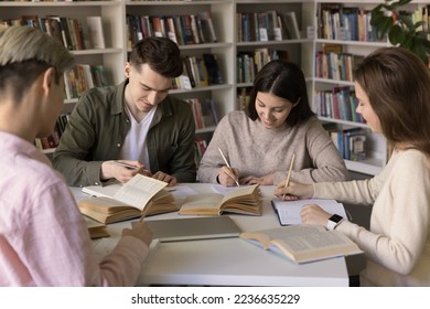 Group of positive young hardworking smart students studying in library, sitting together at open books, writing notes, essay, talking, working on team task, research, preparing report - Powered by Shutterstock