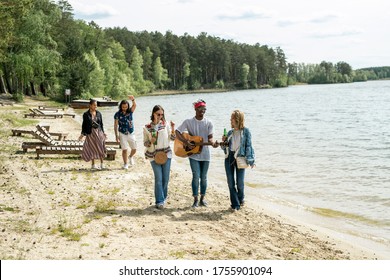 Group Of Positive Young Multi-ethnic Friends Enjoying Beach Stroll While Black Guy Playing Guitar On Move