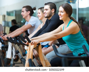 Group of positive young people training on exercise bikes in gym