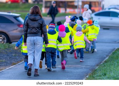 A group of preschoolers - children in selective focus in yellow reflective vests, put on to improve visibility, with a teacher walk along the city street. - Powered by Shutterstock