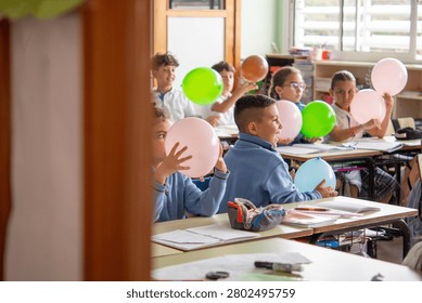 Group of primary school students actively participating in a fun classroom activity using colorful balloons during a lesson.