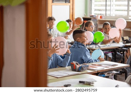 Group of primary school students actively participating in a fun classroom activity using colorful balloons during a lesson.