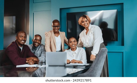 Group of professional colleagues engaging in a collaborative business meeting in a blue-themed office. They are gathered around a laptop, sharing ideas with genuine smiles and a positive team spirit. - Powered by Shutterstock