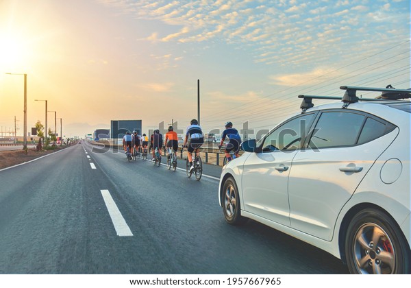 Group of\
professional cyclists training on highway with safety escort car. A\
group of cyclists followed by team\
cars
