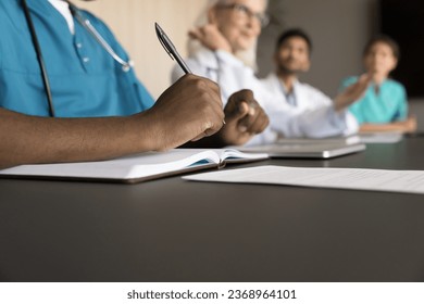 Group of professional doctors meeting at table, discussing treatment cases, medical career. Team of hospital interns training for practitioner professions, writing notes at desk. Cropped shot - Powered by Shutterstock