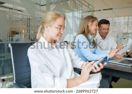 Group of professionals engaged in discussion while one employee checks her phone in a modern office setting during a workday