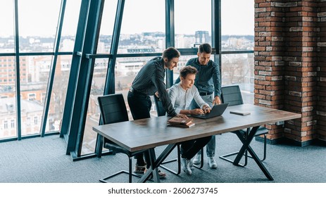A group of professionals engages in a collaborative session near a window, focused on brainstorming and analyzing data using a laptop during a workday in a contemporary office.