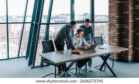 A group of professionals engages in a collaborative session near a window, focused on brainstorming and analyzing data using a laptop during a workday in a contemporary office.