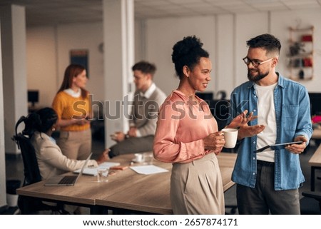 A group of professionals having a conversation and collaborating in an open-plan workspace. The scene conveys collaboration, teamwork, and a friendly atmosphere.