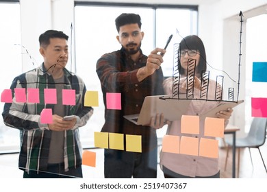 Group of professionals working together on business plan using chart drawings and sticky notes. Team brainstorming and analyzing data for project development in modern office setting. - Powered by Shutterstock