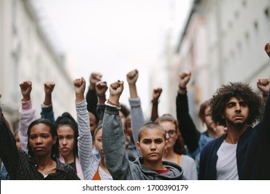 Group of protestors with their fists raised up in the air. Activists protesting on the street. - Shutterstock ID 1700390179