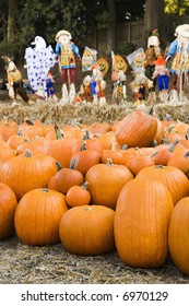 Group of pumpkins sitting on ground at farmers market with yard decorations in background.