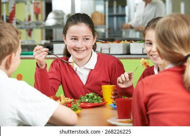 Group Of Pupils Sitting At Table In School Cafeteria Eating Lunch