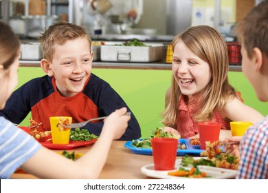 Group Of Pupils Sitting At Table In School Cafeteria Eating Meal