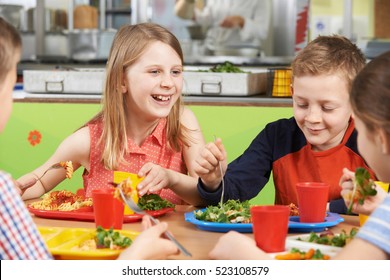 Group Of Pupils Sitting At Table In School Cafeteria Eating Lunch