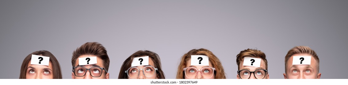 Group of puzzled young people with paper stickers with question mark on foreheads looking up while playing Who Am I game on gray background - Shutterstock ID 1802397649