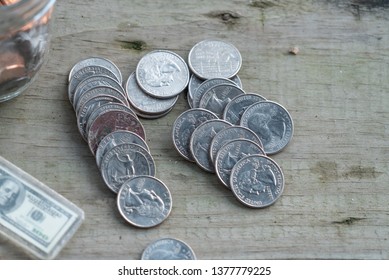 Group Of Quarters Lying On Old Cabin Floor Board With Jar Of Coins And Dollar Key Chain. Finance, Saving, And Retirement Concept On Full Display In Small Town America.