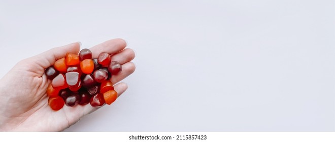Group Of Red, Orange And Purple Multivitamin Gummies In The Hand Isolated On White Background