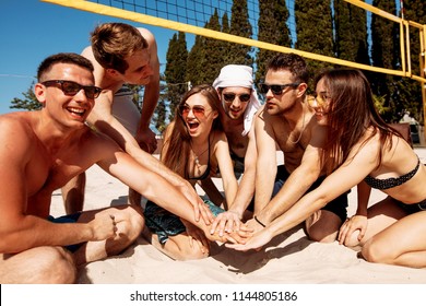 Group of relaxing smiling friends in beach outfit sitting on sand forming a circle, people hands, stacked huddle together- Team people, friendship concept - Powered by Shutterstock