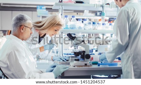 Group of Research Scientists in White Coats are Working with Microscope in a Modern High-Tech Laboratory. Genetics and Pharmaceutical Studies and Researches.
