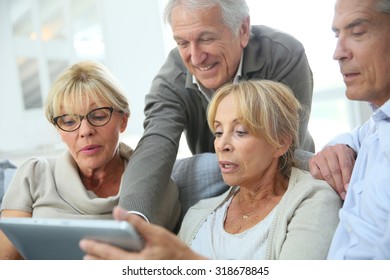 Group Of Retired People Sitting In Sofa And Using Tablet