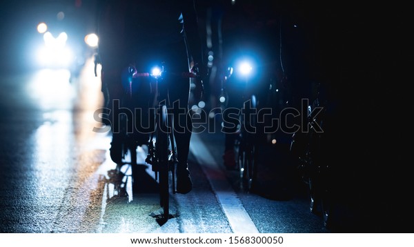 group of road bike riders at night, they turn on\
the headlights.noise in\
image.