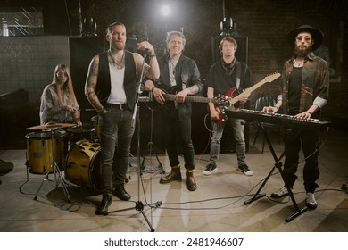 Group of rock male and female musicians playing in rock band posing for camera on stage in modern nightclub - Powered by Shutterstock