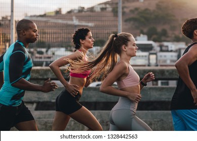 Group Of Runners In Fitness Clothing Running In The City. Young Men And Women Running Together In Morning.