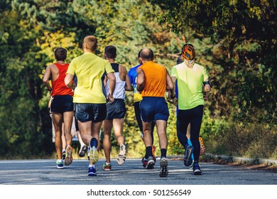 Group Of Runners Marathoners To Run On Asphalt In Autumn Park.yellow Leaves On Trees