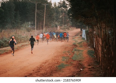 Group Of Runners On A Morning Mass Training In Kenya. Africans Running On Red Roads In Iten City. Running Preparation For Marathon Races