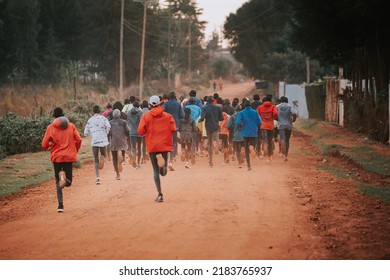 Group Of Runners On A Morning Mass Training In Kenya. Africans Running On Red Roads In Iten City. Running Preparation For Marathon Races