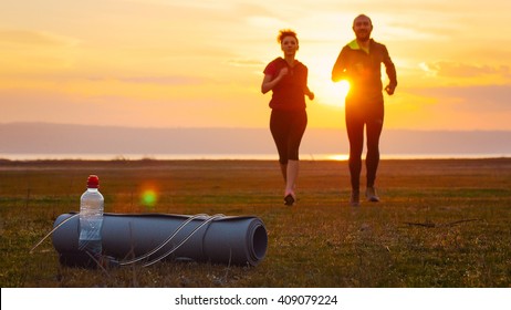 Group Of Runners Training Outdoors Exercising At Sunset In Amazing Landscape Nature. Fit Handsome Athletic Male And Female Working Out For Marathon Run Outside In Summer. Couple, Man And Woman Sport.